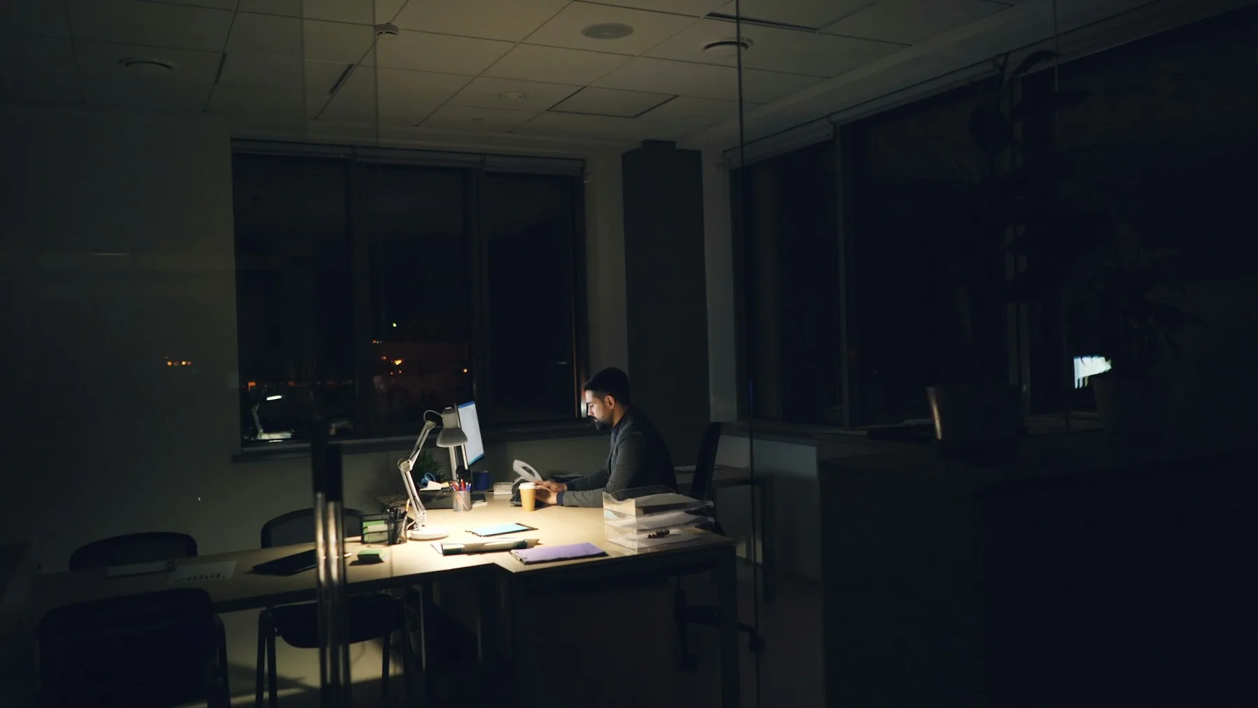 夜、誰もいないオフィスで一人机に向かい、資料を見ている様子